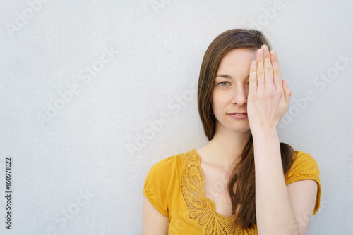 Serious young woman covering one eye