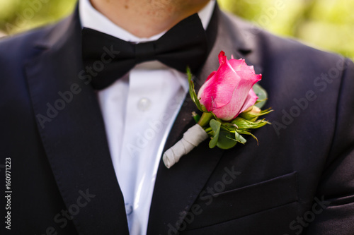 man in a gray suit corrects hand of a red rose boutonniere