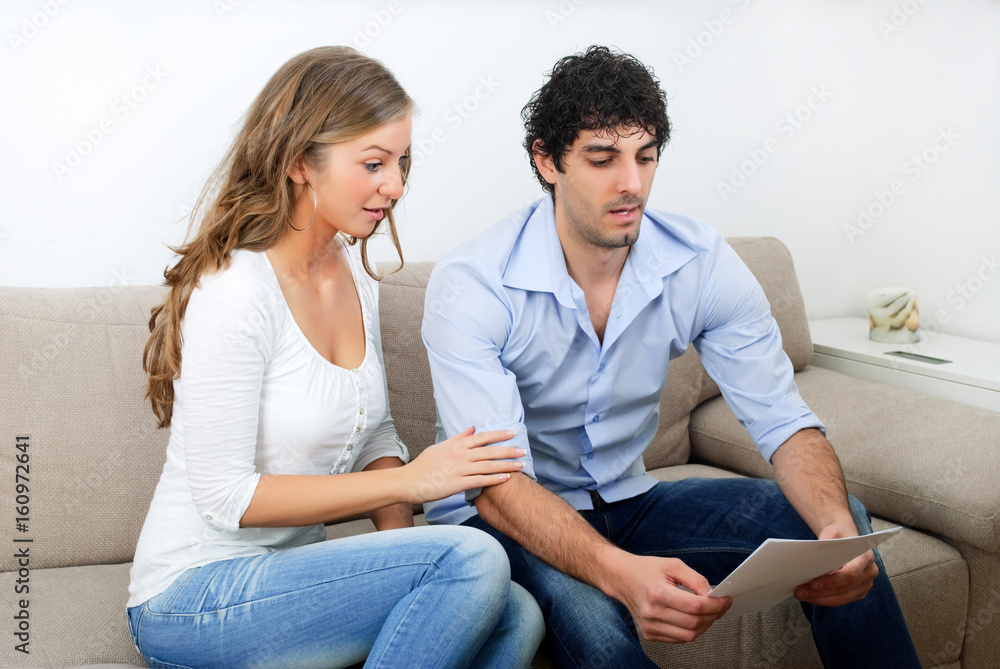 Young couple with bills, surprised at how big the obligations