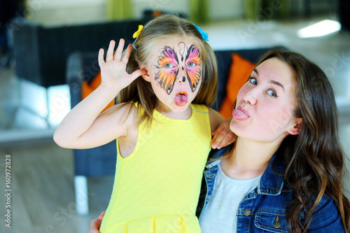 Pretty girl with face painting of a butterfly with babysitter