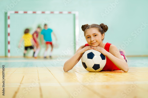 Girl laying on the floor of sports hall with ball