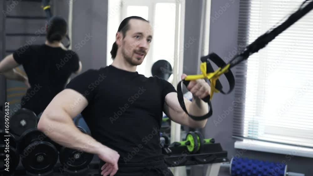 Front view of a man wearing a black sportswear doing one arm push ups with gymnastic rings in a gym. Concept of staying fit and healthy. Real time tilt down tilt up close up shot Front view of a man wearing a black sportswear doing one arm push ups with gymnastic rings in a gym. Concept of staying fit and healthy. Real time tilt down tilt up close up shot