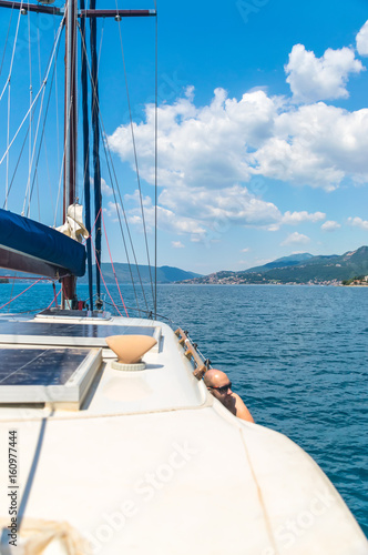 A picturesque landscape is visible from the side of the sailing yacht.