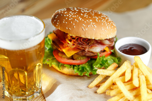 Big tasty burger and fries with beer on foreground on the wooden table