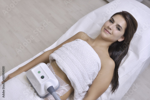 Beautiful young woman getting cryolipolyse treatment in cosmetic cabinet photo