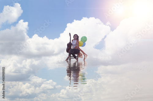 Girl playing guitar while sitting on the chair. Sea reflection and colorful balloons 