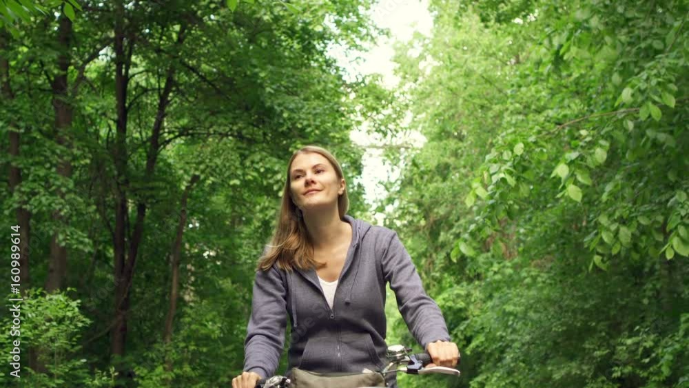 Slow Motion Happy active sportive young woman in hoodies cycling through sunny park on summer's day Slow Motion Happy active sportive young woman in hoodies cycling through sunny park on summer's day