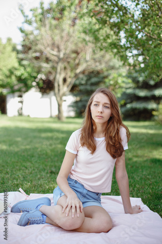 Portrait of young beautiful white Caucasian woman girl sitting on grass in park outside on summer day, toned with retro filters, film effect, candid lifestyle