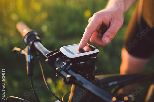 A young brunette guy on a mountain bike uses a cycling computer, a navigator in the field sunset of the day