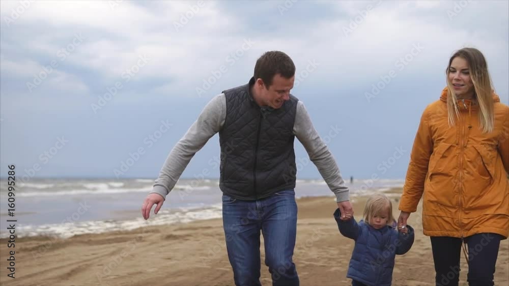 Young family enjoying walking on the beach. Man, woman little girl and boy. Mother and father holding girl in hands. Happy times together Young family enjoying walking on the beach. Man, woman little girl and boy. Mother and father holding girl in hands. Happy times together