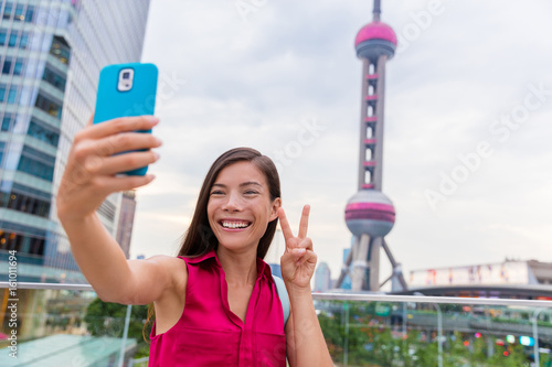 Photography Asian tourist girl taking a selfie smartphone picture at a famous Shanghai landmark in the financial district of Pudong in China