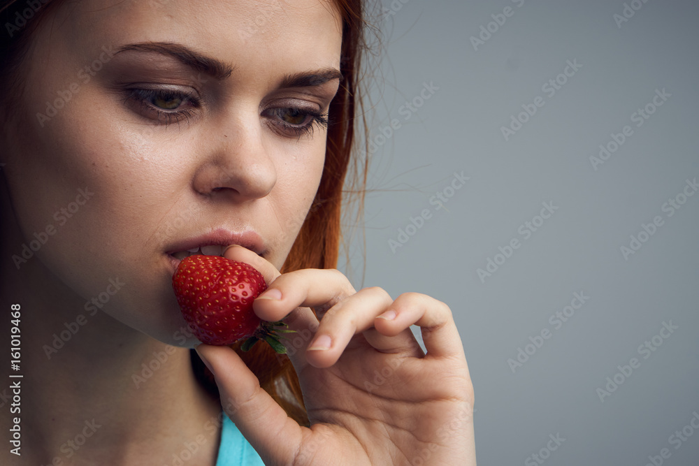 Woman eating strawberries, strawberries, beautiful woman having bitten off strawberries on gray background portrait Woman eating strawberries, strawberries, beautiful woman having bitten off strawberries on gray background portrait