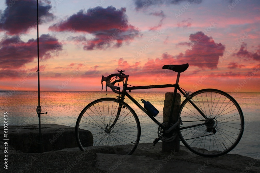 Silhouette of a bike standing beside a dock by the beach with a sunset background Silhouette of a bike standing beside a dock by the beach with a sunset background