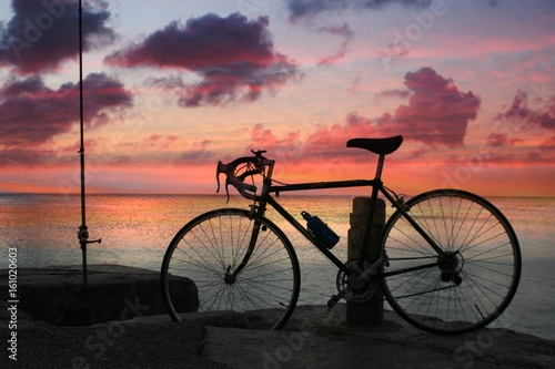 Fototapeta Naklejka Na Ścianę i Meble -  Silhouette of a bike standing beside a dock by the beach with a sunset background