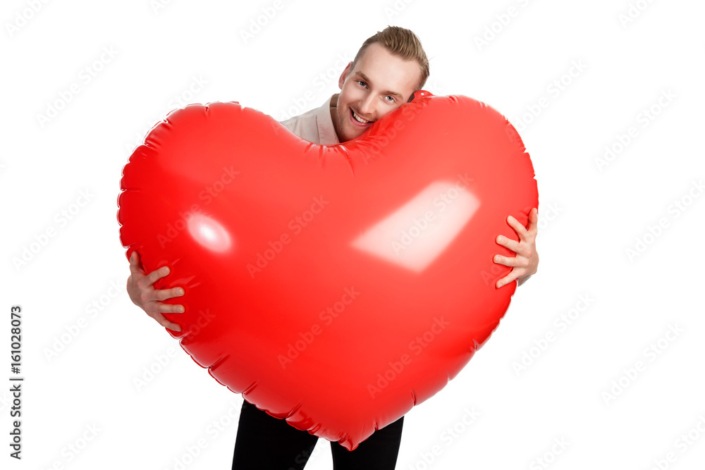 Man standing with a huge oversized heart with a big smile on his face wearing a white shirt. White background. Man standing with a huge oversized heart with a big smile on his face wearing a white shirt. White background.