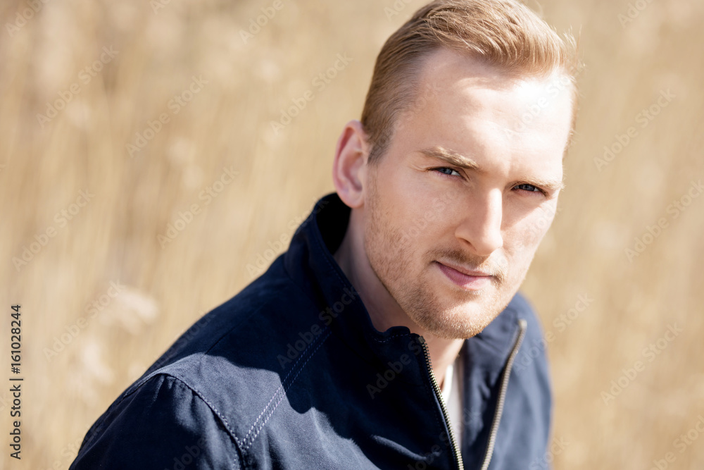Portrait of a focused man standing outside with a wheat field behind him on a sunny spring day, Portrait of a focused man standing outside with a wheat field behind him on a sunny spring day,