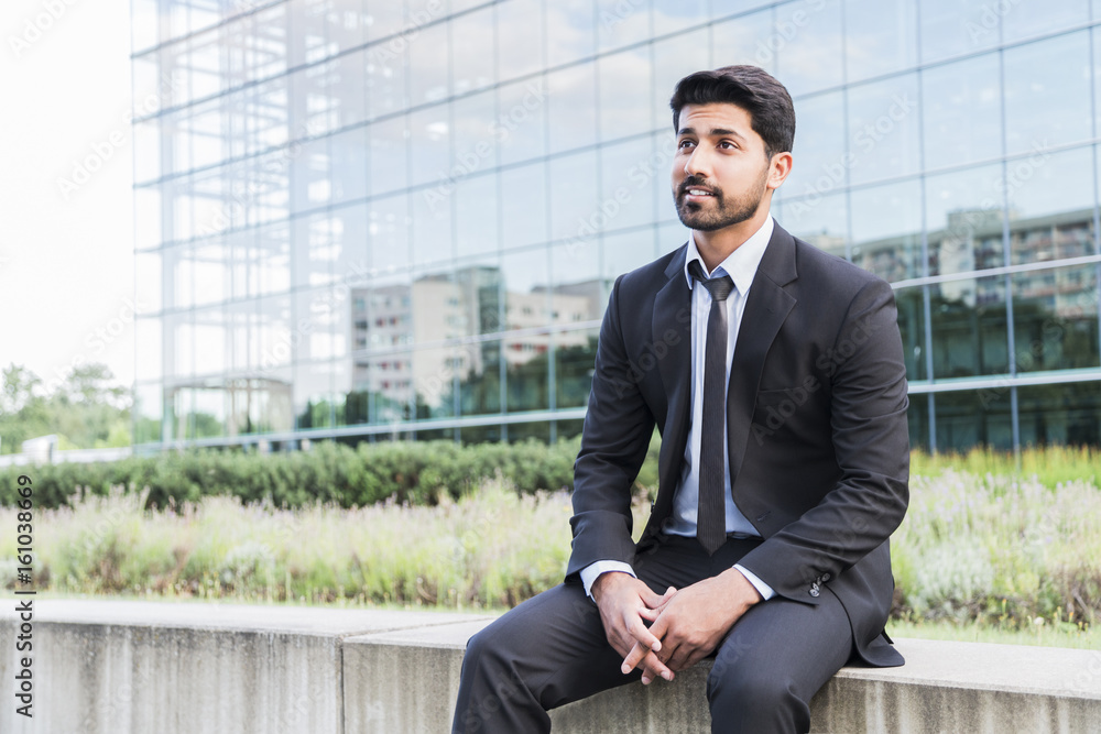 Successful businessman or worker sitting in suit near glass building