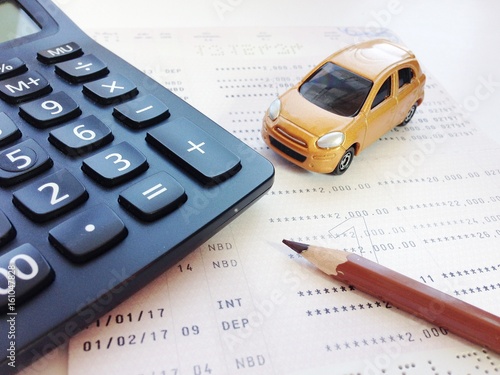 Business, finance, savings, banking or car loan concept : Miniature car model, pencil, calculator and savings account passbook or financial statement on white background