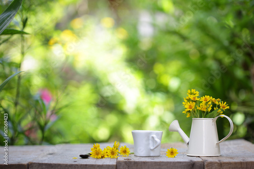 Yellow flower in white pot and coffee cup on wooden table
