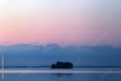 A lake with a small island on which the trees grow. Sunset landscape.