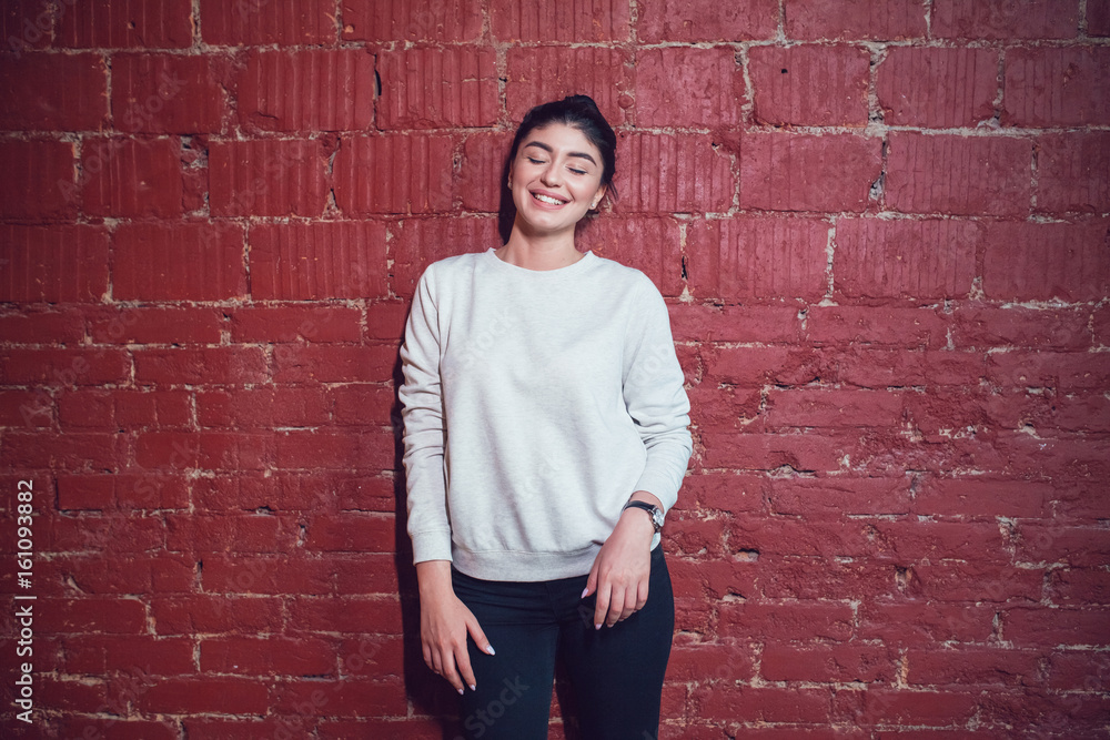 Attractive brunette in a gray sweatshirt stands on a red brick wall background. Mock-up. Attractive brunette in a gray sweatshirt stands on a red brick wall background. Mock-up.