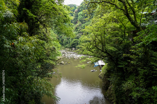View of Takachiho gorge from above seeing river  boats at pier and rocky shore through lush green trees and mountain background