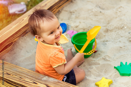 Billede på lærred Happy little girl playing in a sandbox on the playground