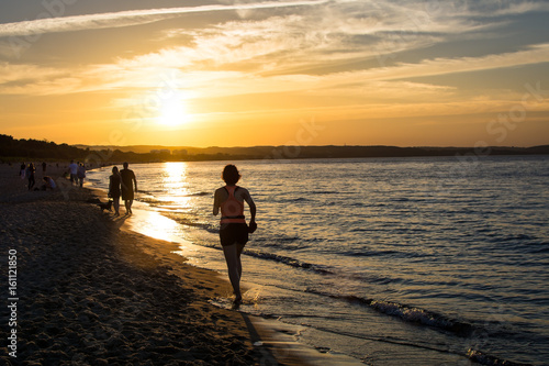People walking and jogging along Gdansk city beach in Jelitkowo under setting sun. Gdańsk, Poland, 19.06.2017