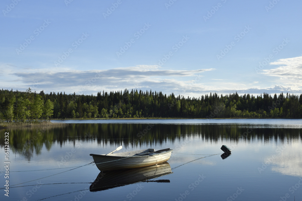 Boat moored on a calm lake with forest and blue sky in background.