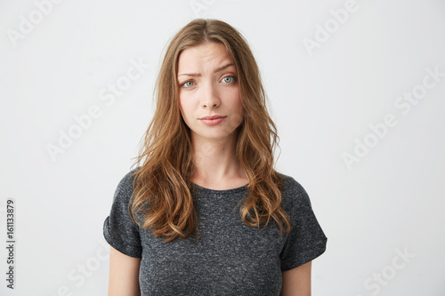 Displeased young beautiful girl looking at camera raising one eyebrow over white background.