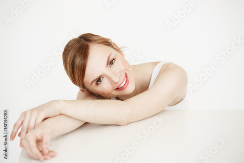 Happy beautiful blonde girl with healthy clean skin smiling looking at camera sitting at table over white background. Facial treatment.