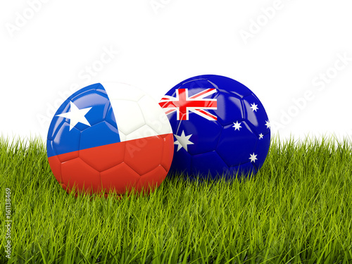 Two footballs with flags of Chile and Australia on green grass