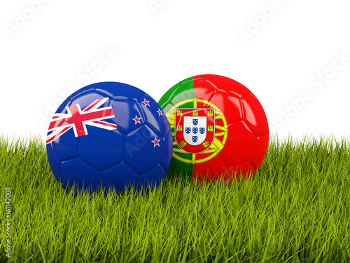Two footballs with flags of New Zealand and Portugal on green grass