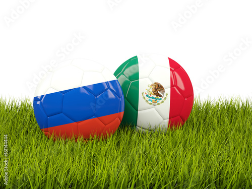 Two footballs with flags of Russia and Mexico on green grass