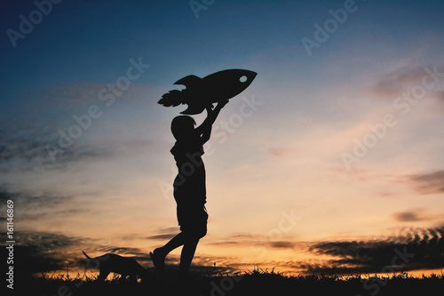 Silhouette boy holding a rocket paper and playing with little dog on the sky sunset color of vintage tone