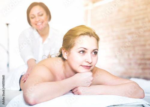 Massagist is doing massage of back and loin to smiling young woman