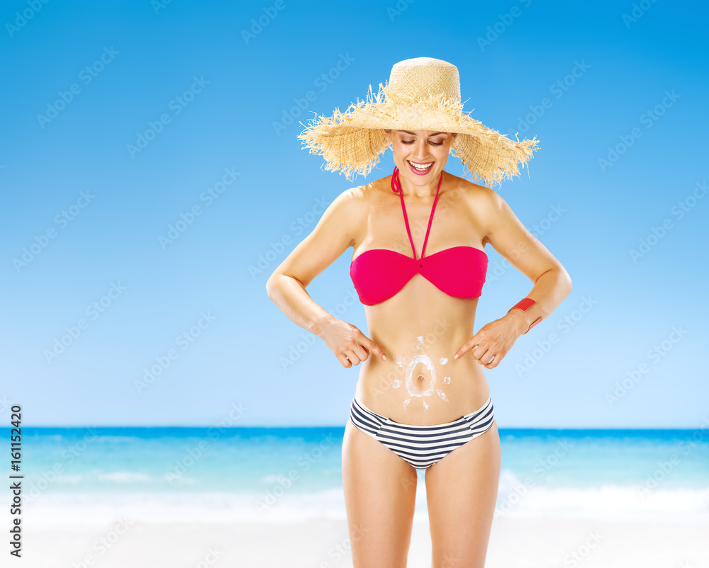 woman on seashore pointing on sun drawn by spf creme on stomach