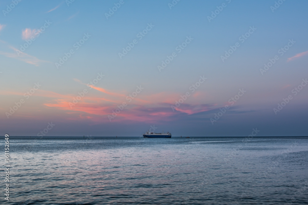 Big ship standing on the horizon under pink sunset cloud.  Roadstead of Gdansk port.