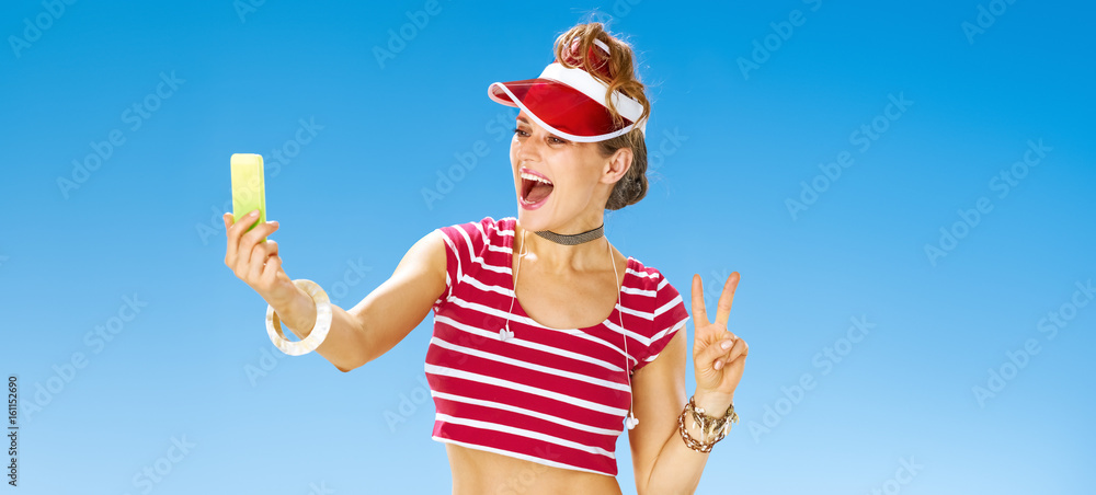 woman on beach taking selfie with cellphone and showing victory