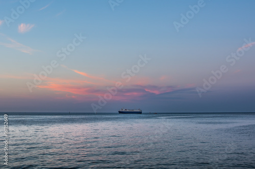 Fototapeta Big ship standing on the horizon under pink sunset cloud