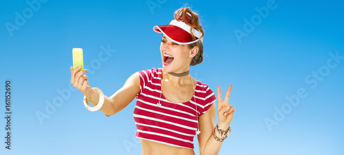 woman on beach taking selfie with cellphone and showing victory