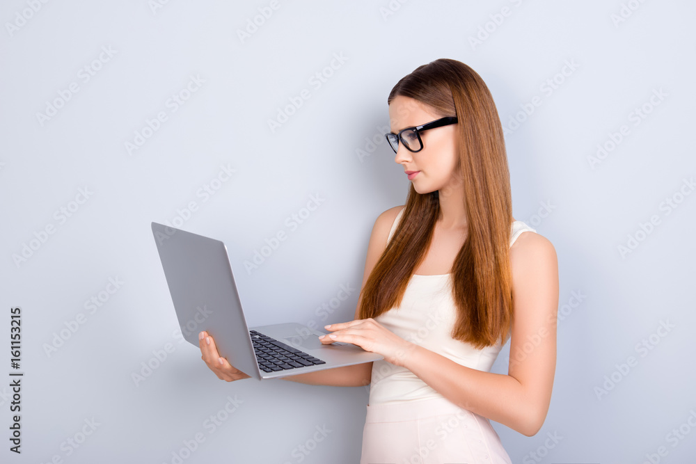 Success and work, study concept. Young serious lady journalist is working on her laptop, wearing casual clothes and glasses, on pure light background Success and work, study concept. Young serious lady journalist is working on her laptop, wearing casual clothes and glasses, on pure light background