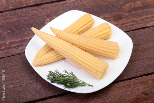 Mini Corn cob preserved on plate on wooden board. photo