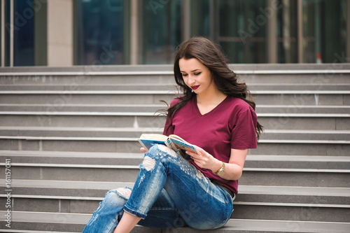 Beautiful woman reading a book on the steps of the building.