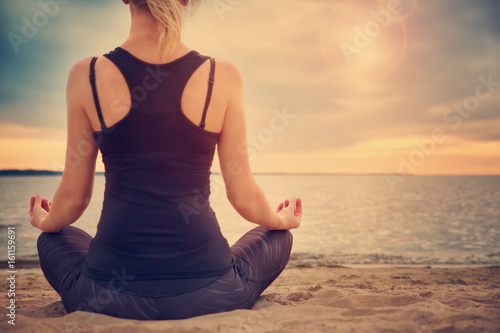 young woman sitting on the beach and practicing yoga