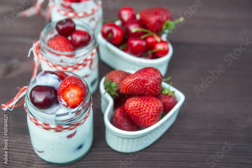 yogurt with Cherry and strawberries  square. Berries of blueberries and strawberries are scattered on the table.