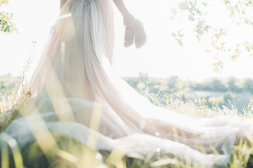 Bride in wedding dress holds shoes against sun. fine art photography