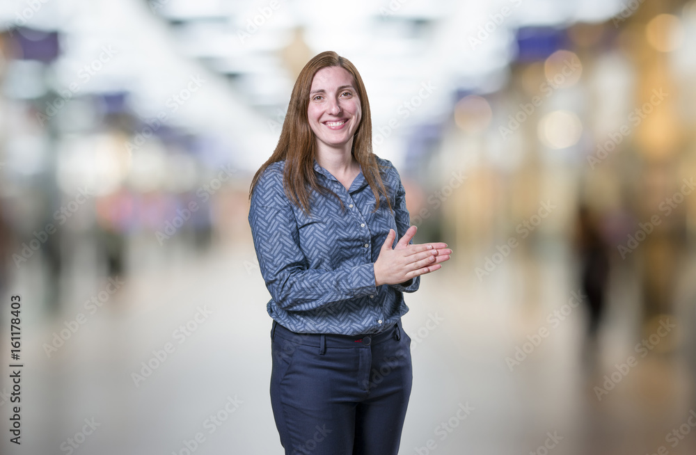 Pretty young businesswoman is clapping over blur background.