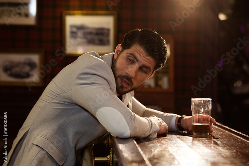 Quadro su tela Young drunk man sitting at the counter in a pub