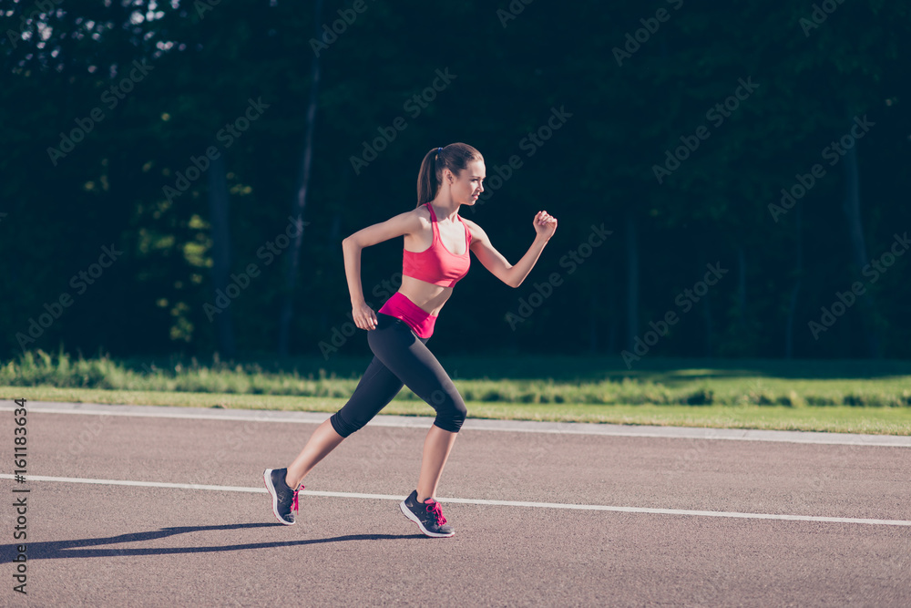 Young lady trainer running outdoors, training for marathon run. Beautiful fitness model, in fasionable sports outfit, jogging sneakers, so fit and fast!